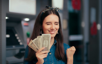 Girl having financial success holding dollars in front of a bank