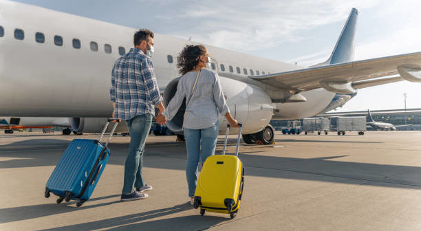 Back view of man and woman wearing protective masks and walking with suitcases. Trip concept